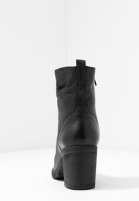 Botas negras de tobillo con un upper suave, acentos texturizados con patrón de serpiente y un tacón robusto. Incluyen una lengüeta trasera para facilitar su colocación.