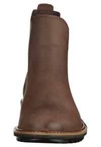 Bottine en cuir marron avec une texture lisse, un bout arrondi et des accents cousus. Elle possède une semelle en caoutchouc profilée basse.