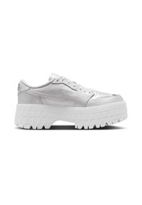 Baltie Nike kedas ar teksturētu ādas virsu, plakanu kurpju auklu slēgšanu un masīvu platformas zoli, kas rotāta ar režģa rakstu.