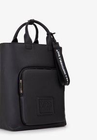 Borsa a tracolla nera in texture con tasca frontale con zip, due manici arrotondati e un cinturino da polso etichettato "IO SONO UNA BORSA RESPONSABILE."