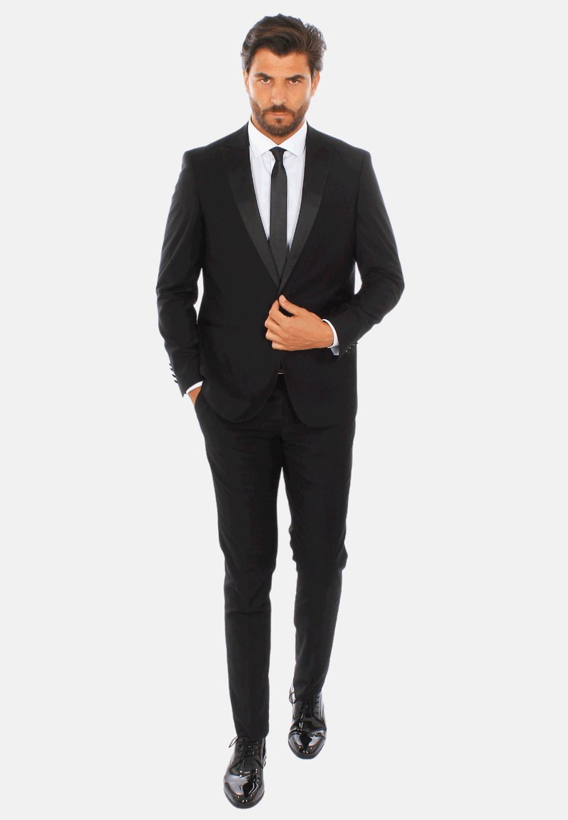 Tuxedo nero con rever in satin, dalla forma aderente, abbinato a una camicia bianca e cravatta nera. Scarpe eleganti nere lucide completano il look.