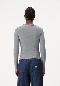 Långärmad topp i grå och vita ränder, med rund halsringning och smal passform, tillsammans med mörkblå denimbyxor.