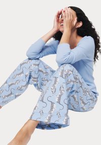 Un haut à manches longues bleu clair associé à un pantalon de pyjama bleu avec un imprimé de léopards blancs soulignés de noir. Texture de tissu douce.