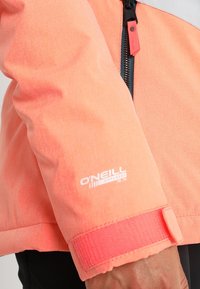 Chaqueta de color coral con una textura suave, cierre de cremallera y puños de velcro. Presenta un logo de O'Neill en la manga.