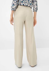 Pantaloni a gamba larga in tessuto beige chiaro, caratterizzati da una texture liscia, un design minimalista e tasche posteriori discrete.