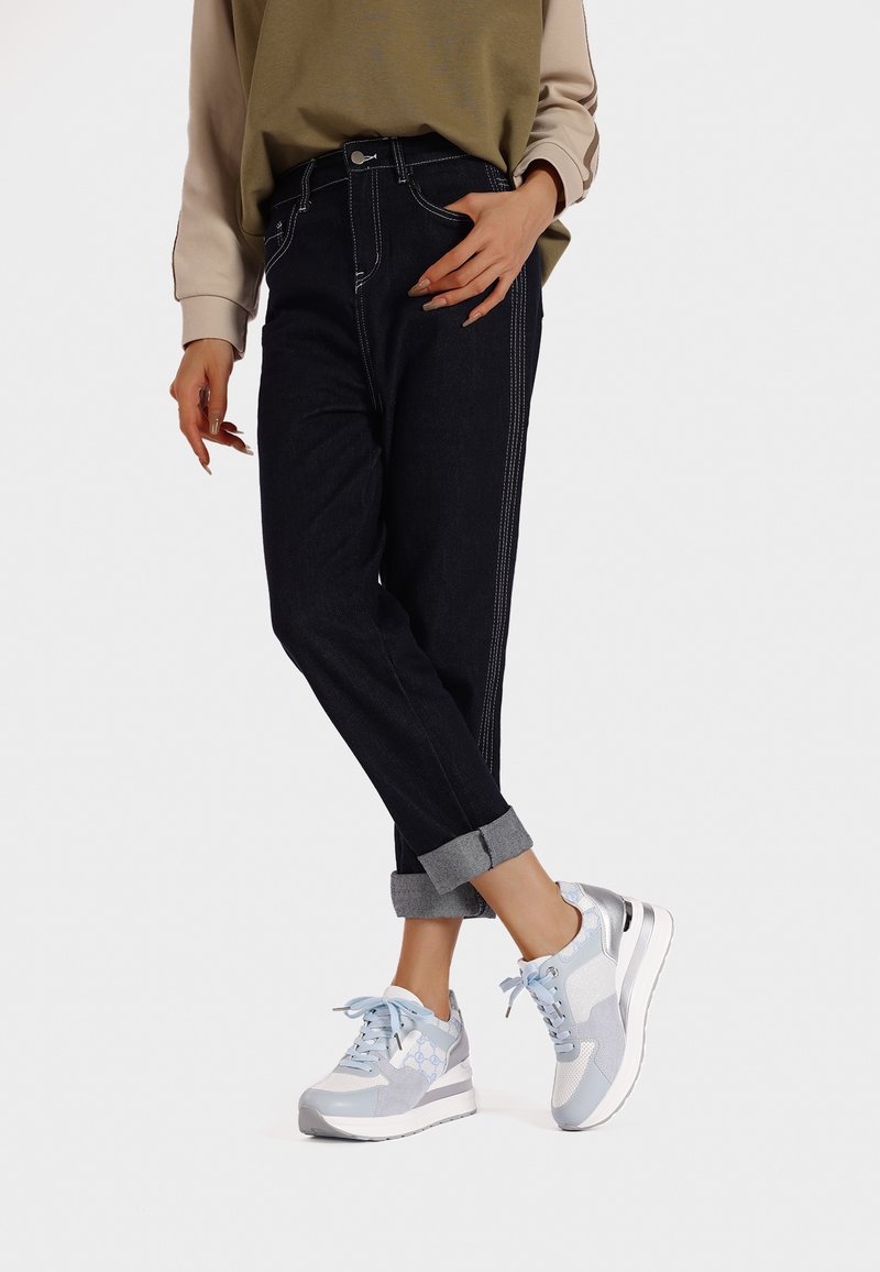 Jeans alti blu scuro con cuciture bianche a contrasto, risvoltini sulle caviglie, abbinati a sneaker grigie chiare e blu con dettagli in rete.