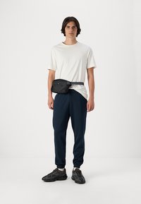 Hvid kortærmet t-shirt, marineblå joggers med elastiske manchetter, sort bæltetaske om livet og mørke sportsko.
