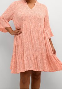 Robe à imprimé floral rose avec un décolleté en V, un col ruffle et des manches évasées trois-quarts. Présente une silhouette en cascade et fluide. Tissu doux.