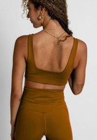 Top corto deportivo marrón con tirantes gruesos, que presenta una espalda amplia y una tela suave, combinado con leggins de talle alto a juego.
