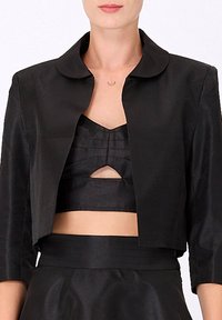 Veste noire courte avec un col arrondi et des manches trois-quarts, fabriquée à partir d'un tissu lisse. Présente un design minimaliste.