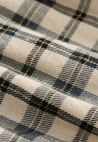 Tessuto a quadri intrecciato in beige, nero e grigio con fili metallici. Presenta quadri a contrasto e una finitura morbida e tessurizzata.