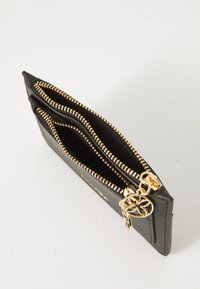 Portefeuille noir à fermeture éclair en matériau texturé, doté de deux compartiments avec des fermetures éclair dorées et un pendentif décoratif attaché.