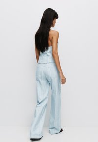 Completo due pezzi in denim azzurro chiaro con top senza spalline e pantaloni larghi a gamba larga con righe verticali e tasche posteriori visibili.