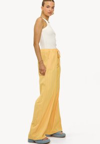 Gele verticaal gestreepte wijde broek met een elastische tailleband, gecombineerd met een aansluitend wit tanktop en blauwe platform sandalen.