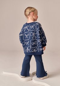Sweat-shirt bleu marine avec motif de nœuds blancs et poignets côtelés, associé à un pantalon évasé assorti avec ourlets festonnés et petits nœuds.