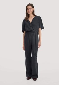 Schwarzer Jumpsuit mit Wickeldesign, kurzen Ärmeln, einem taillierten Gürtel und weitem Bein, gefertigt aus einem glatten, leichten Stoff.