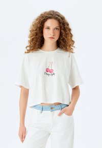 Weißes, kurzes T-Shirt aus weichem Stoff mit einer Grafik von zwei Kirschen mit einer pinken Schleife und dem Schriftzug "Cherry Baby" in Schwarz.