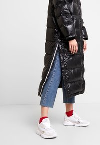 Černá péřová bunda s lesklým povrchem, vystavená s vertikálním prošíváním a bočními zipy. V kombinaci s zkrácenými džíny a bílými teniskami s červenými akcenty.