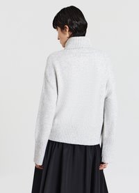 Hellgrauer, übergroßer Pullover mit hohem Rippkragen und langen Ärmeln. Der gerippte Saum sorgt für Textur. Trägt einen schwarzen Rock.