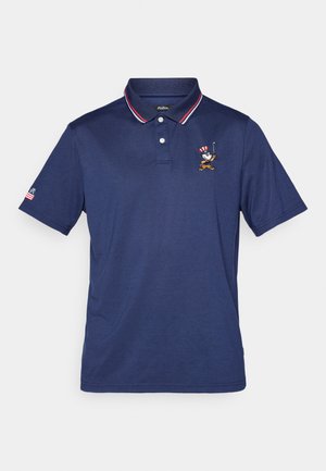 Marineblå poloskjorte laget av bomull med krage, med røde og hvite stripete detaljer og en brodert figur på brystet.