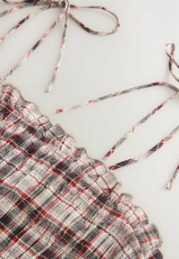 Plaid cropped top valmistettu kevyestä kankaasta, jossa on röyhelöreunat, säädettävät nauhat sekä punainen, harmaa ja beige värimaailma, jossa on tekstuuria.
