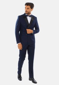 Smoking doppiopetto blu navy con rever in satin nero, camicia bianca e papillon nero. Completato da scarpe eleganti nere lucide.