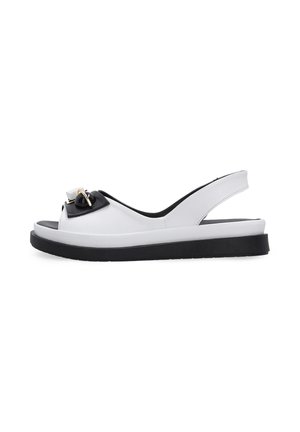 White leather slingback sandal with black sole and decorative black and gold buckle on the front strap.