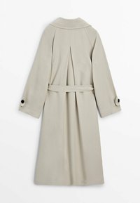 Beżowy trencz z kołnierzem, długimi rękawami i paskiem. Posiada plisy z tyłu oraz mankiety zapinane na guziki. Gładka tekstura o minimalistycznym wzornictwie.