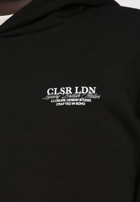 Fato preto feito de algodão macio, apresentando texto do logótipo bordado em branco, com detalhes "CLSR LDN" e "Crafted in Soho".