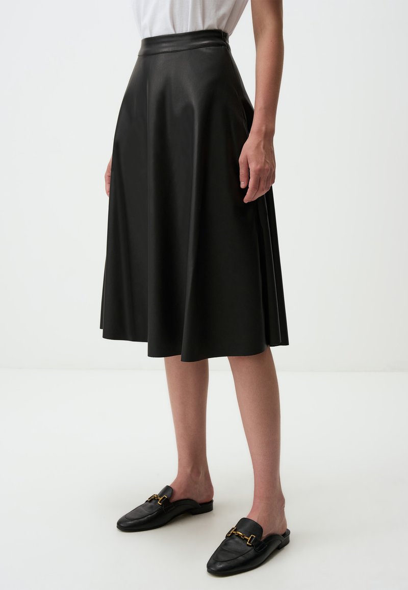 Jupe en simili cuir noir à taille haute et silhouette en A, dotée de plis pour plus de volume et associée à des chaussures noires à enfiler.