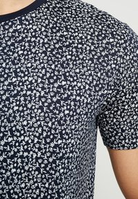Námořnická modrá tričko s krátkým rukávem s bílým květinovým vzorem, kulatým výstřihem a měkkou, texturovanou látkou.