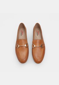 Tan leren loafers met een gladde textuur, voorzien van een goudkleurige kettingaccent op de bovenkant. De binnenvoering heeft "Bata RedFOAM" gedrukt.