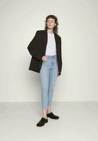 Blazer oversized preto, t-shirt branca, jeans skinny azul claro e sapatos slip-on pretos. Design minimalista com uma textura suave.