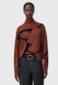 Sweter z golfem z dzianiny w kolorze rdzy z przeskalowanymi czarnymi wzorami logo, z prążkowanymi mankietami i luźnym krojem, zestawiony z czarnymi skórzanymi spodniami.