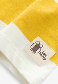 Gelb-weißer gestreifter Stoff mit einer strukturierten Oberfläche, versehen mit einem genähten Etikett mit einer Biene-Grafik und dem Text "bee happy."