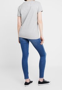 Maglietta grigia a maniche corte con una vestibilità rilassata, abbinata a jeans skinny blu e sneakers nere. Tessuto morbido, design semplice, senza decorazioni.