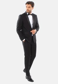 Tuxedo nero con rever in satin, abbinato a una camicia bianca e cravatta a farfalla nera. Scarpe eleganti nere lucide. Design slim-fit.