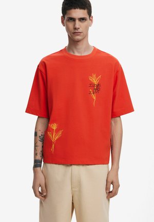 Red short-sleeved t-shirt made of cotton, featuring yellow embroidered floral designs and text, with a relaxed fit and crew neckline.
