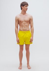 Κίτρινα μαγιοπ με ελαστική μέση και κορδόνι, σχεδιασμένα για άνεση. Με λεία υφή, μήκος μέχρι τη μέση του μηρού, χωρίς ορατά σχέδια.