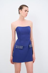 Robe bleue sans bretelles avec un corsage ajusté, un ourlet évasé et des poches décoratives ornées de clous métalliques. Texture lisse et design minimaliste.
