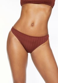 Gestreifte Bikini-Hose in tiefem Rostrot. Verfügt über einen tief geschnittenen Bund, elastischen Taillenbund und eine glatte Textur. Einfaches, minimalistisches Design.