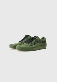 Zapatillas de gamuza verde con cordones negros, que presentan una franja lateral negra en contraste, una suela gruesa y detalles de costura blanca.