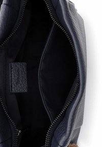 Granatowa skórzana torba z gładkim wnętrzem, zamknięciem na zamek i małą, teksturowaną metką. W przestronnym wnętrzu nie widać żadnych kieszeni.