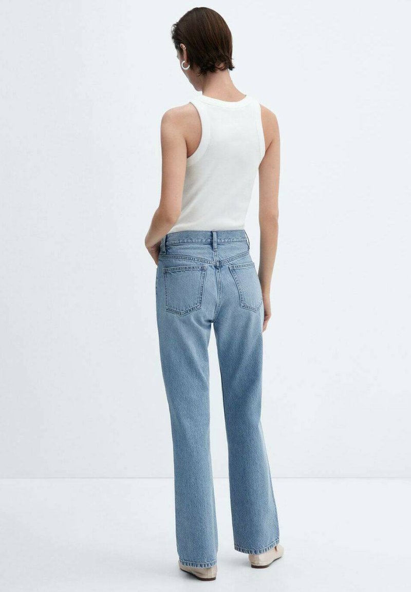 Hellblaue, ausgestellte Jeans aus Denim mit hoher Taille und zwei Gesäßtaschen. Kombiniert mit einem weißen ärmellosen Top.