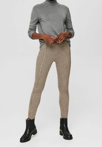 Beige en bruin geruite legging van stretchstof, aansluitend ontwerp, gecombineerd met zwarte enkellaarzen en een grijze coltrui.