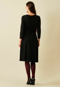 Musta mekko, jossa on kolme neljännes hihaa, levenevä hame ja istuva vyötärö. Yhdistetty burgundinvärisiin leggingseihin ja mustiin korkokenkiin. Sileä rakenne.