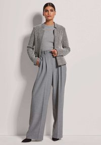 Graue Wollhose mit weiten Beinen, kombiniert mit einer strukturierten, enganliegenden Jacke in Schwarz und Weiß. Beide Teile zeichnen sich durch klare Linien und maßgeschneiderte Details aus.