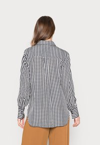 Camisa de botão em padrão gingham preto e branco com mangas longas, colarinho e um ajuste relaxado, apresentando um detalhe de pregas nas costas.
