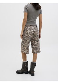Shorts al ginocchio con motivo leopardato, dal taglio rilassato, abbinati a stivaletti neri alla caviglia con fibbie e una maglietta grigia a maniche corte a costine.