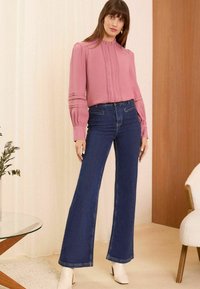 Rozā blūze ar krokotām detaļām un puffed piedurknēm, apvienota ar tumši zilajiem platiem džinsiem un baltiem potīšu zābakiem. Mūsdienīgu dizaina elementu klātbūtne.